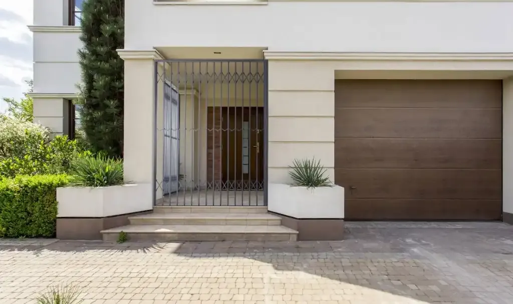 A grey trellis gate closed across a recessed front entrance beside a garage door.