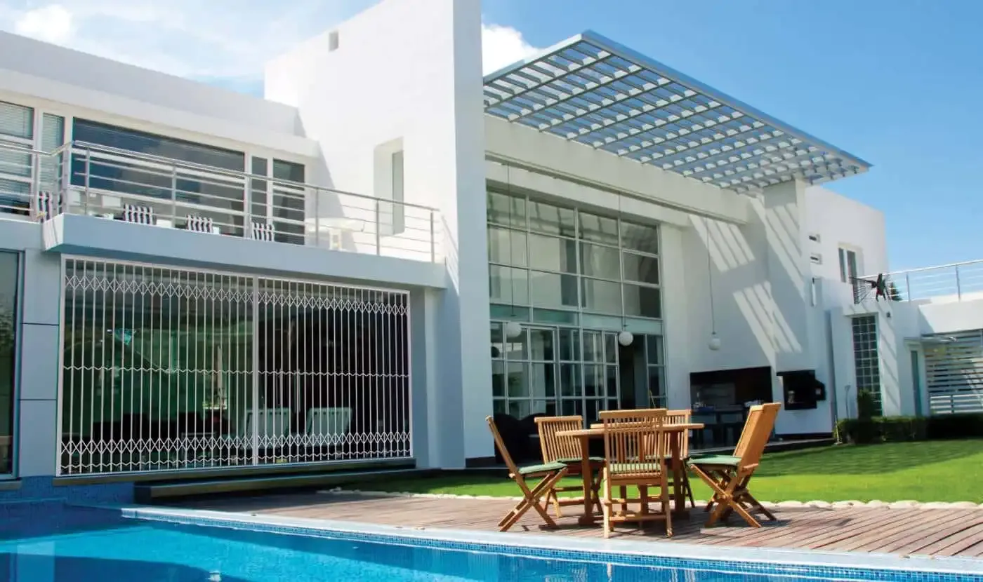 White trellis gates drawn across the ground-floor stacking doors of a double-storey home beside a pool.