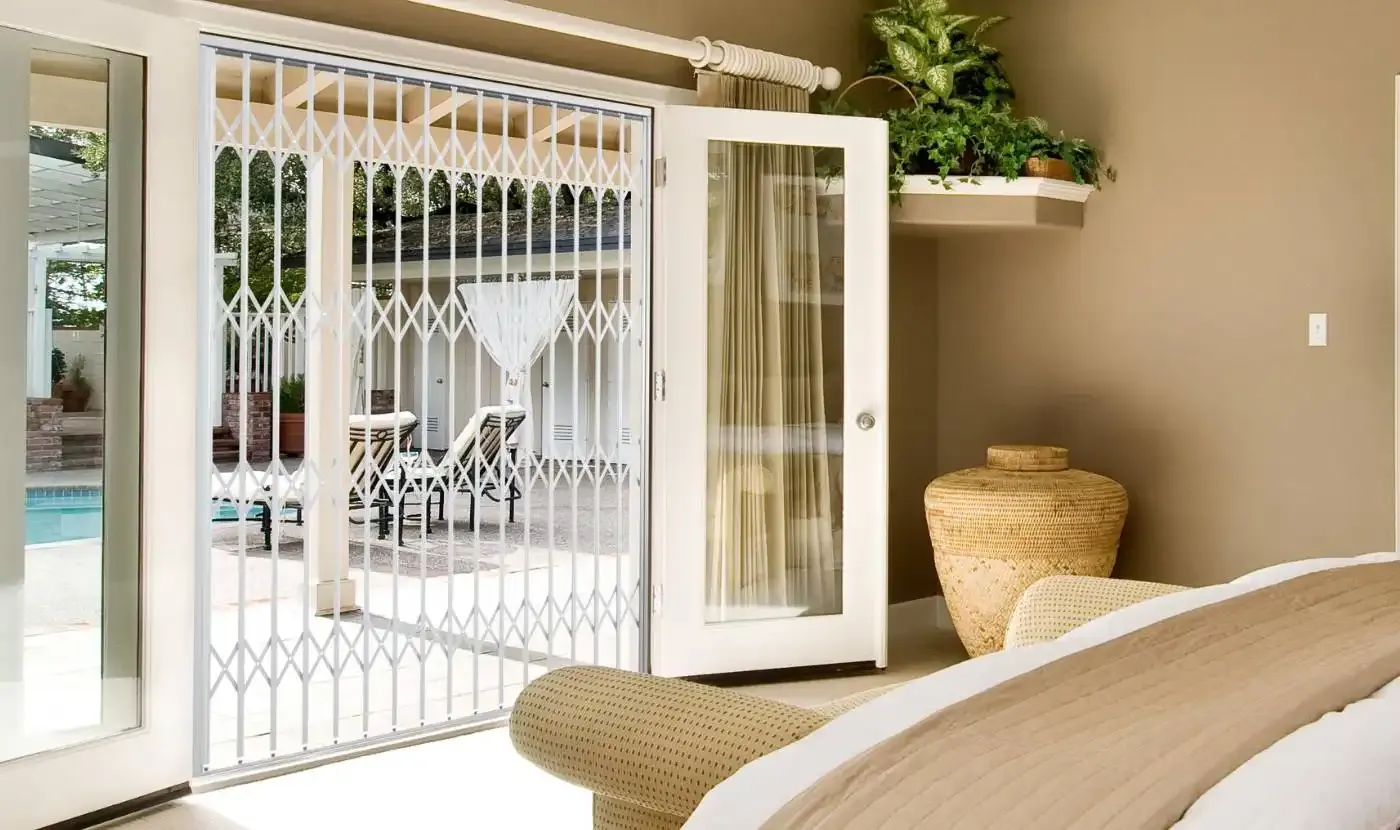 A white trellis gate closed across bedroom doors that open onto a pool patio, with the door behind it standing open.
